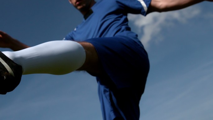 足球运动员在蓝天下慢动作踢球