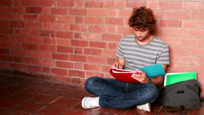 在大学里，一个学生靠着墙坐着读课本