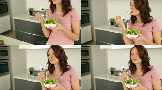 漂亮女人在厨房里吃着一碗健康沙拉