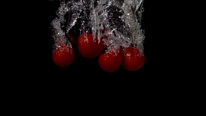 在黑色背景的慢镜头中，小番茄落在水中