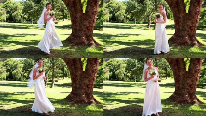 在一个阳光明媚的日子里，兴奋的新娘手捧花束在公园里对着镜头微笑