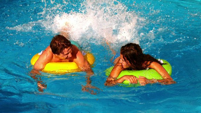 年轻夫妇戏水和有乐趣在游泳池充气环在慢动作