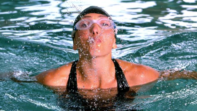有趣的女性游泳运动员在游泳池向镜头喷水的慢镜头