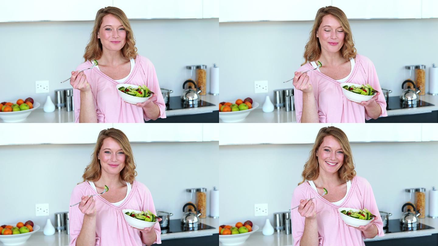 漂亮女人站在厨房里吃着一碗沙拉