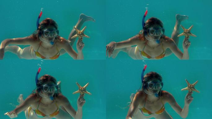 在慢镜头中，一个女人戴着通气管，拿着海星在水下
