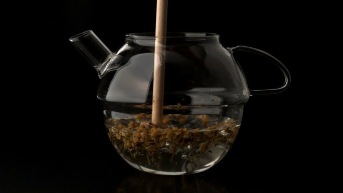 木棒搅拌茶壶的水和松散的茶在慢动作