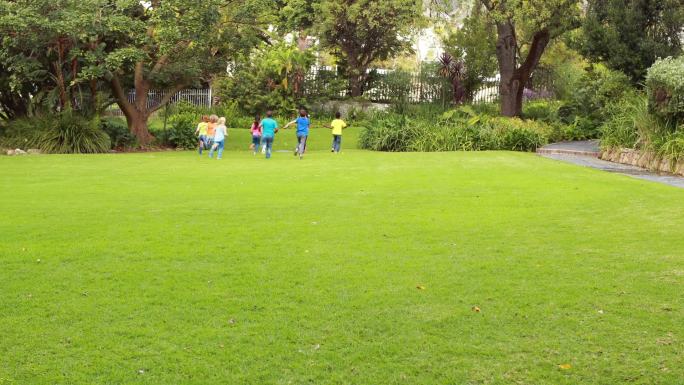 一排可爱的小学生在小学外面的草地上赛跑