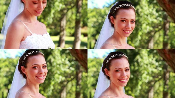 在一个阳光明媚的日子里，新娘手捧花束在公园里对着镜头微笑