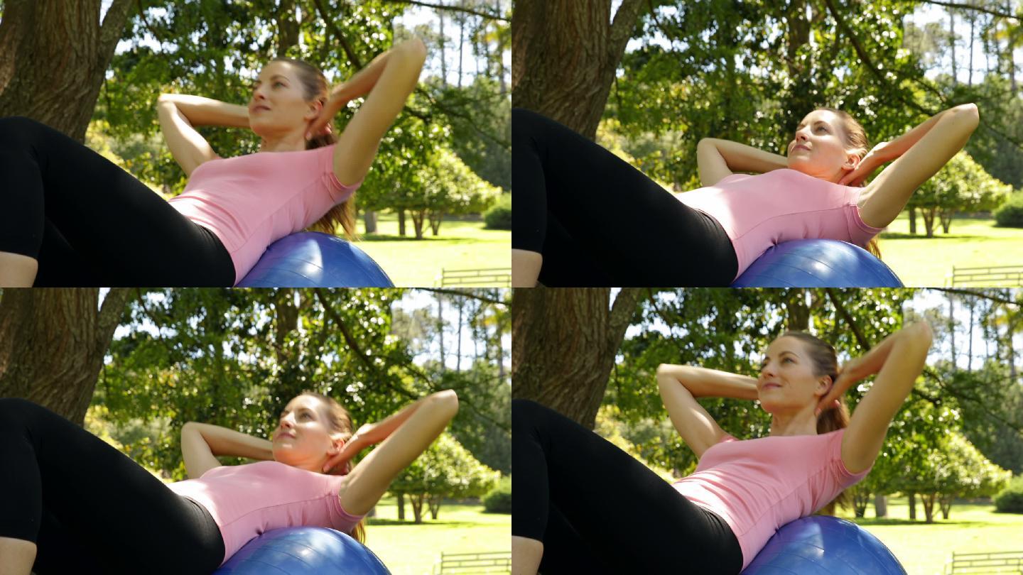 在一个阳光明媚的日子里，健身的女人在公园里的健身球上做仰卧起坐