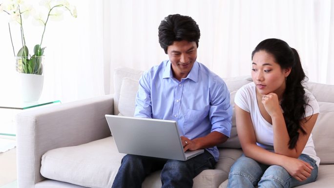 一个亚洲男人在客厅里给女朋友看笔记本电脑上的东西