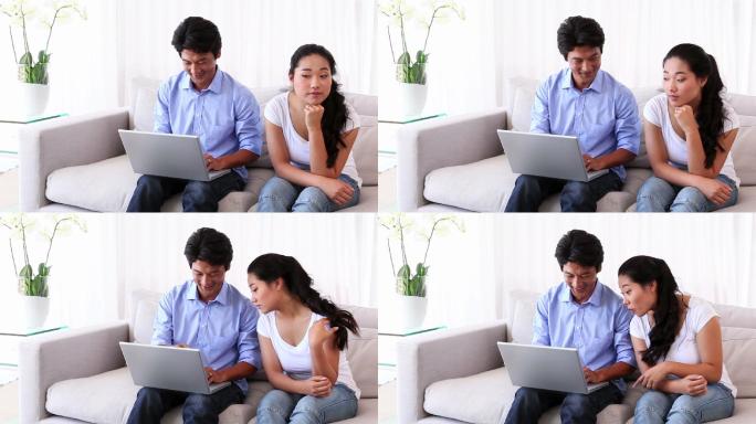 一个亚洲男人在客厅里给女朋友看笔记本电脑上的东西