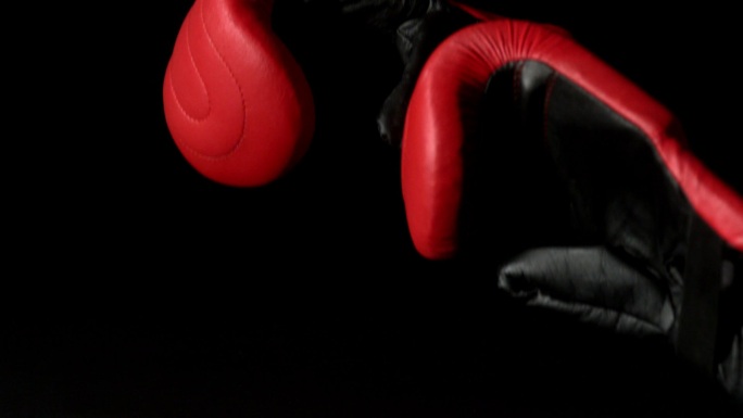 在慢镜头中，红色拳击手套落在黑色背景上