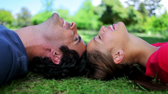一对微笑的情侣一起躺在乡间的草地上