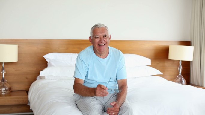 老人坐在床上对着镜头微笑在早上在家里的卧室里
