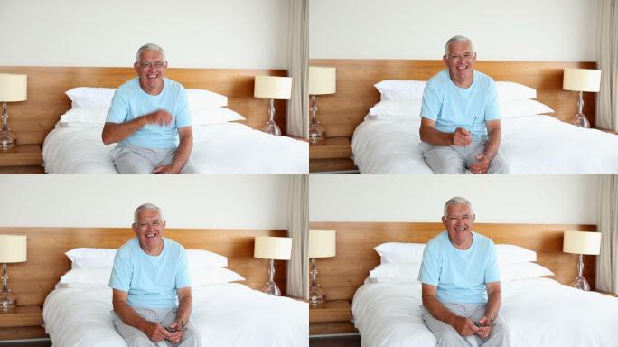 老人坐在床上对着镜头微笑在早上在家里的卧室里