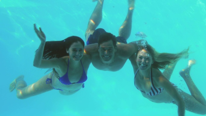 三个朋友在度假时跳进游泳池里挥手