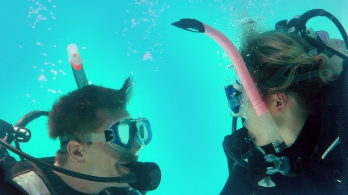 一对穿着潜水装备的夫妇在水下看着对方的慢动作
