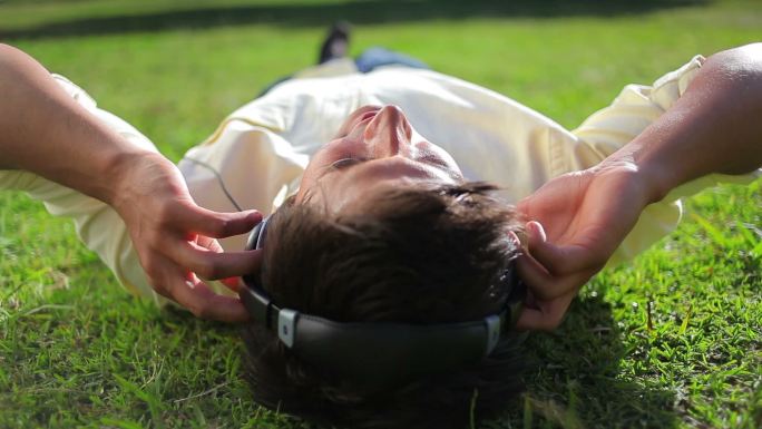 一个平静的人躺在公园的草地上听着音乐