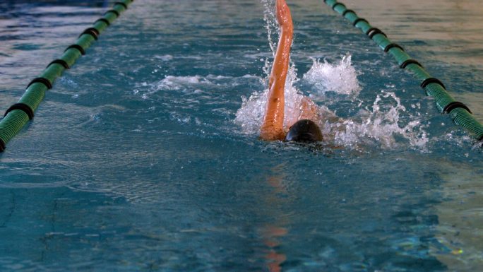健康的女子游泳运动员在游泳池慢动作仰泳