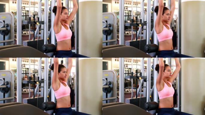 身材苗条的黑发女子在健身房的举重机上锻炼手臂