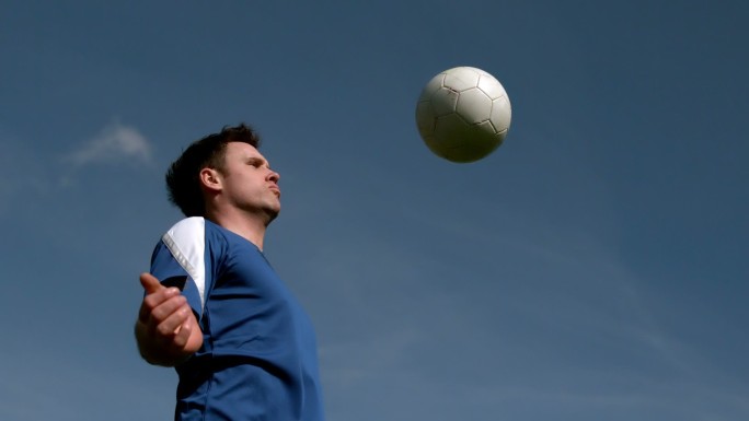 足球运动员在蓝天下用慢镜头用胸触球