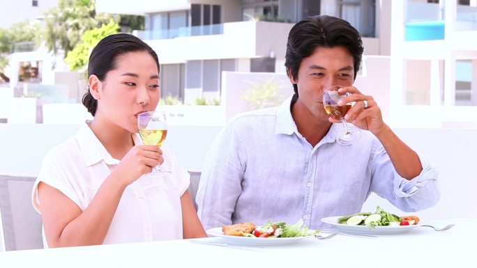 一对亚洲夫妇在外面的阳台上用白葡萄酒进餐