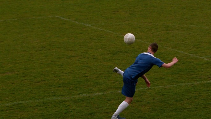 穿蓝色衣服的足球运动员在球场上用慢动作踢球