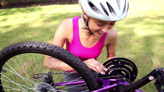 一个健康的女孩在一个阳光明媚的日子修理她的自行车链条