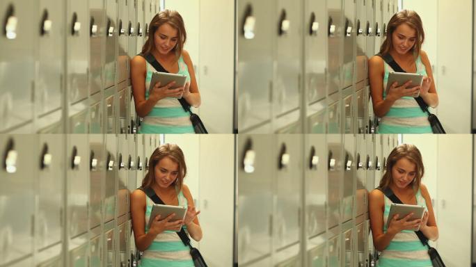 漂亮的学生在大学储物柜旁边的走廊里用平板电脑