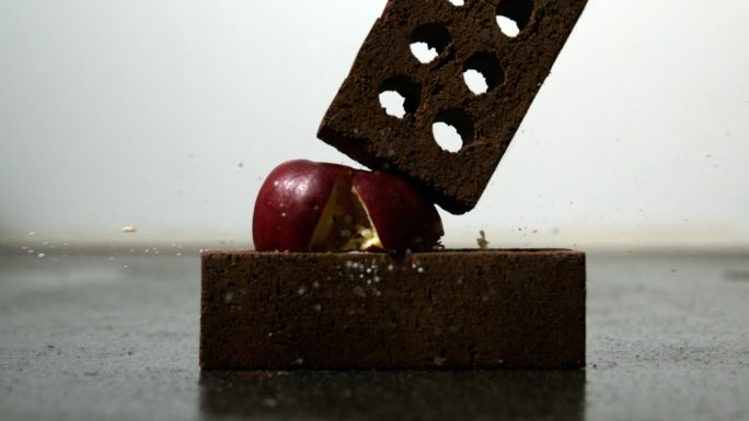 用慢镜头把苹果压在两块砖头之间