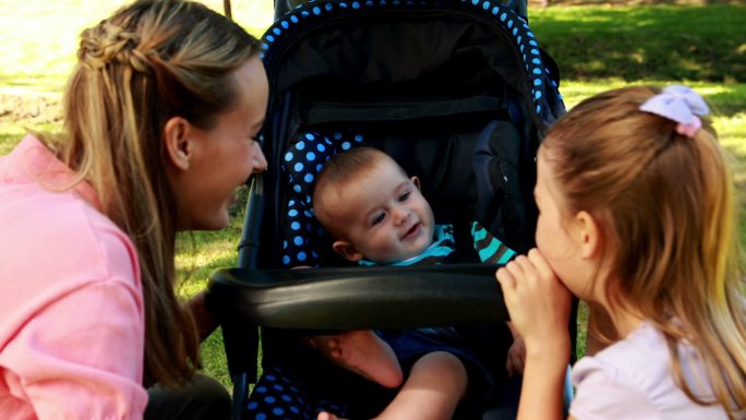 在一个阳光明媚的日子里，妈妈和女儿在公园里推着婴儿车玩