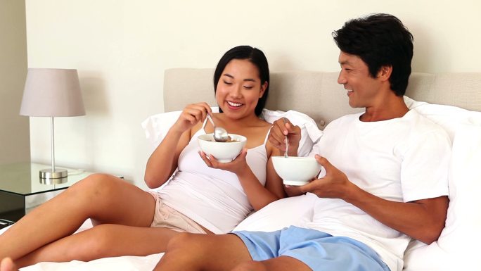 一对夫妇在卧室的床上吃碗麦片