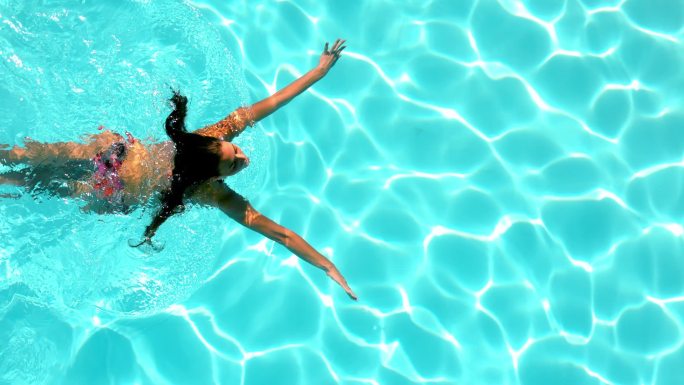 在一个阳光明媚的日子里，黑发女子慢动作地游过游泳池