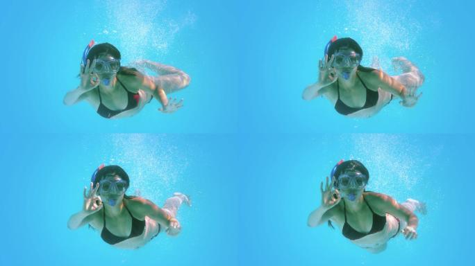 黑发女子在水下游泳，戴着通气管，慢动作做ok手势