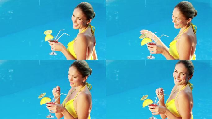 在一个阳光明媚的日子里，穿着比基尼的金发美女在泳池边享受鸡尾酒