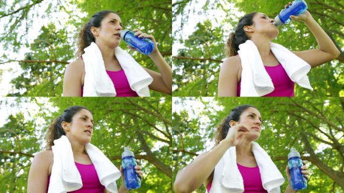 在一个阳光明媚的日子里，一名妇女在公园里锻炼后，擦拭她的额头和喝水