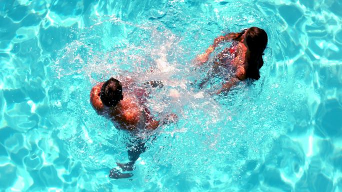 一对夫妇在游泳池里玩得很开心，在慢动作中溅起水花