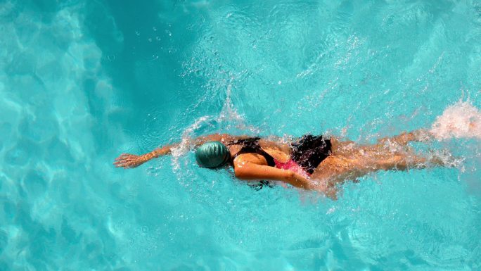 健康的女游泳运动员在游泳池中缓慢地向前划水