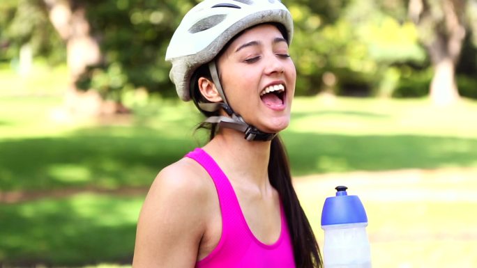 健康的女孩在一个阳光明媚的日子里骑自行车喝水