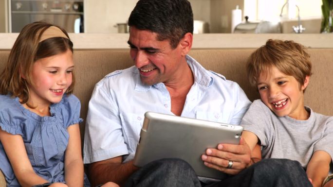 可爱的孩子们在客厅沙发上和父亲一起使用平板电脑