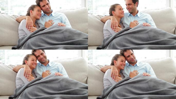 一对可爱的夫妇躺在沙发上，盖着毯子在客厅里聊天