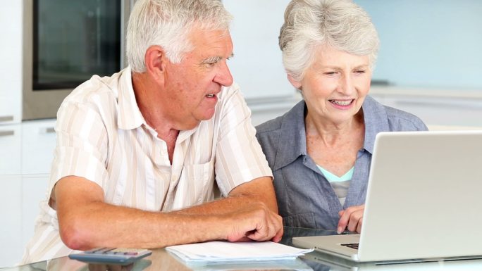 一对老年夫妇在厨房里用笔记本电脑支付账单