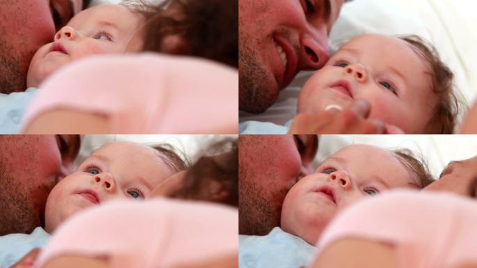 穿着蓝色婴儿服的男婴正在卧室的床上被快乐的父母亲吻