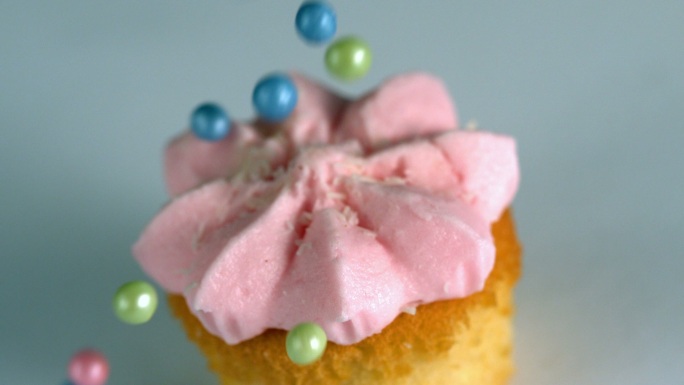 慢镜头里，糖球落在带粉色糖霜的纸杯蛋糕上