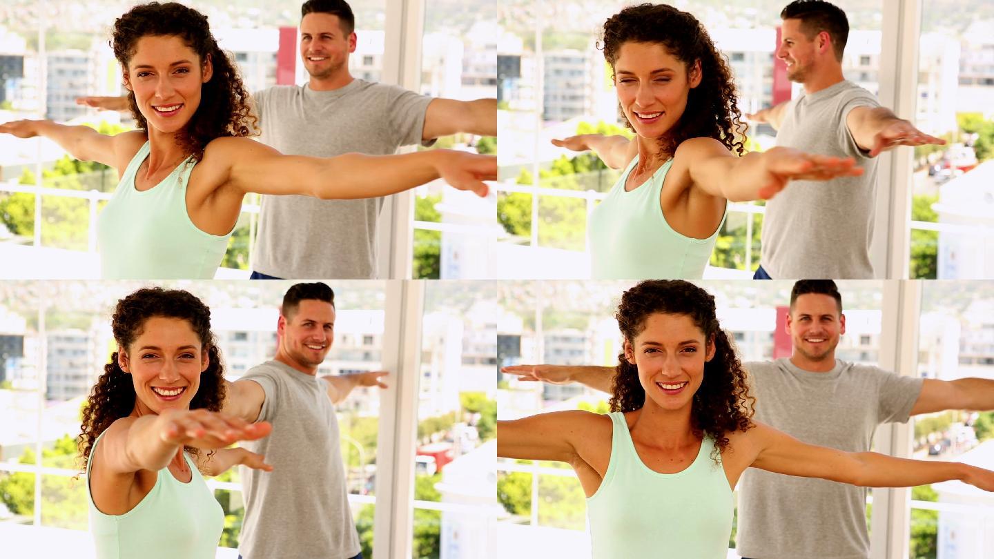 一对幸福的情侣对着镜头微笑，在健身房做瑜伽