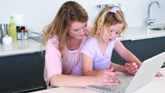 漂亮的母亲和女儿一起在厨房里使用笔记本电脑