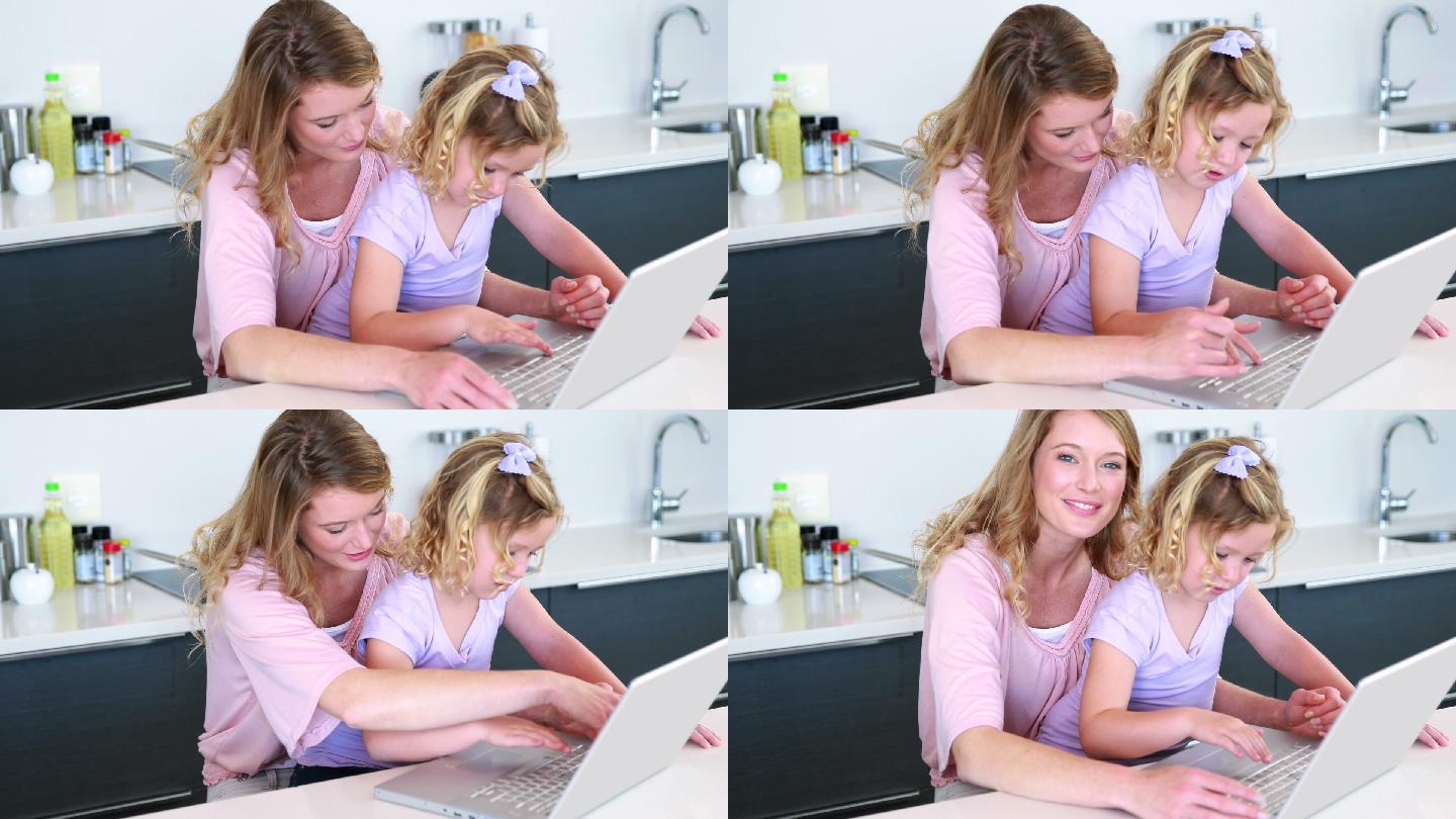 漂亮的母亲和女儿一起在厨房里使用笔记本电脑