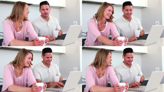 一对幸福的夫妇一起使用笔记本电脑，在家里的厨房里喝咖啡
