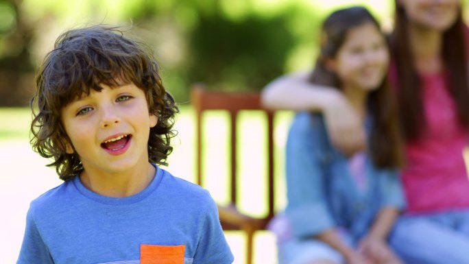 Little boy waving at camera with family behind on 