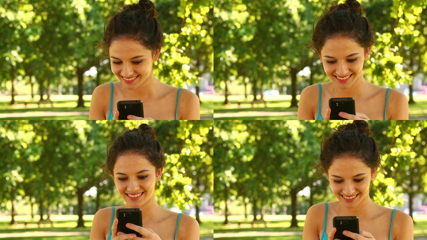 在一个阳光明媚的日子里，一个漂亮的黑发女子在公园里发短信